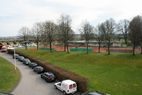 Geparkte Autos entlang der Zufahrt, dahinter die Tennisplätze