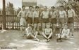 Historisches Gruppenfoto von Sportlern in Sportkleidung vor einem Holzzaun