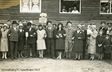 Historisches Gruppenfoto von Männern und Frauen vor einem Holzgebäude