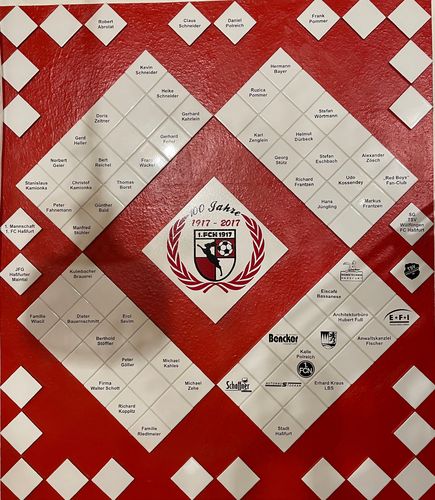 Fliesenwand mit rot-weißen Rautenfliesen, in der Mitte das Vereinswappen