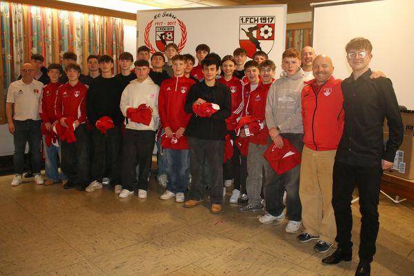 Die U17 der Dreiberg Kickers in roten Trainingsjacken vor dem Vereinsbanner