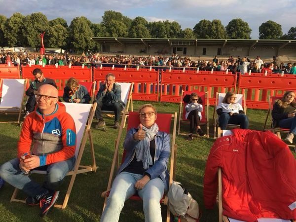 Zuschauer in Liegestühlen auf dem Rasen vor der voll besetzten Tribüne