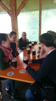 Personen mit Bierkrügen an einem Tisch unter einem Holzdach
