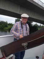 Mann mit Schirmmütze und Kamera an Deck unter einer Brücke