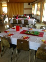FC-Saal mit langen, weiß eingedeckten Tischreihen, roten Tischläufern und Servietten, Holzstühlen und Fenstern mit Vorhängen