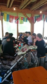 Gruppe an einem langen Tisch unter einem Holzdach mit Länderfähnchen