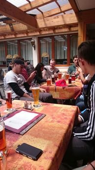 Gruppe an gedeckten Tischen mit Getränken unter einem Holzdach