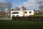Vereinsheim hinter einer Hecke und einer Rasenfläche