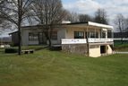 Vereinsheim mit Terrasse, davor Rasenfläche und Bäume