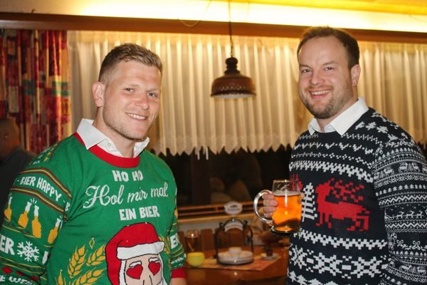 Zwei Männer in Weihnachtspullovern, einer mit Bierkrug
