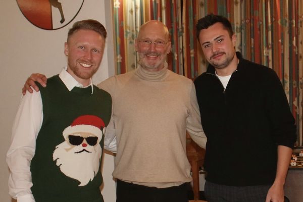 Drei Männer, einer im Weihnachtspullover mit Weihnachtsmann-Motiv