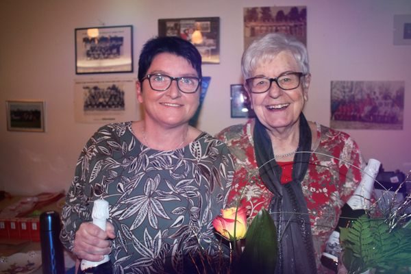 Zwei Frauen mit Sektflasche und Blumen vor einer Wand mit Mannschaftsfotos