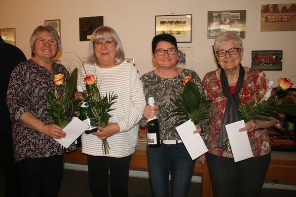 Vier Frauen mit Blumen und Umschlägen vor einer Wand mit Mannschaftsfotos