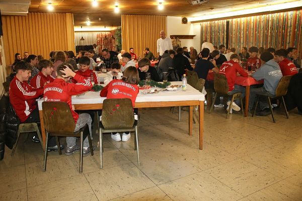 Blick in den Saal mit Jugendlichen in roten Jacken an langen Tischen