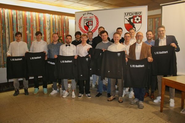 Spieler präsentieren neue schwarze Trikots mit der Aufschrift „1. FC Haßfurt“ vor dem Vereinsbanner