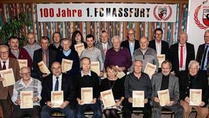 Gruppenfoto geehrter Mitglieder mit Urkunden vor dem Banner „100 Jahre 1. FC Hassfurt“
