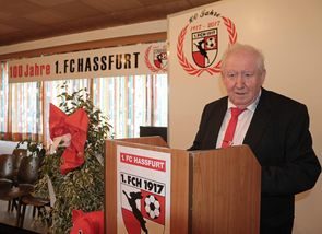 Redner am Rednerpult mit Vereinswappen vor dem Jubiläumsbanner