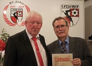 Zwei ältere Herren mit Urkunde vor dem Jubiläumslogo und dem Vereinswappen