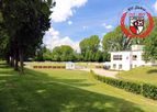 Rasenfläche mit Hecke und Vereinsheim, oben rechts das Jubiläumslogo „100 Jahre 1917–2017“