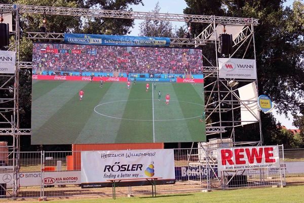LED-Großleinwand auf einem Gerüst mit Sponsorenbannern, auf dem Bildschirm läuft ein WM-Spiel
